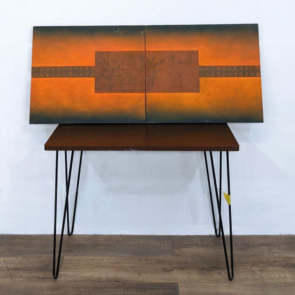 Alt text 1: Reperch diptych artwork featuring two bright orange canvases with a central Asian-style image, displayed on a wooden table against a white wall.