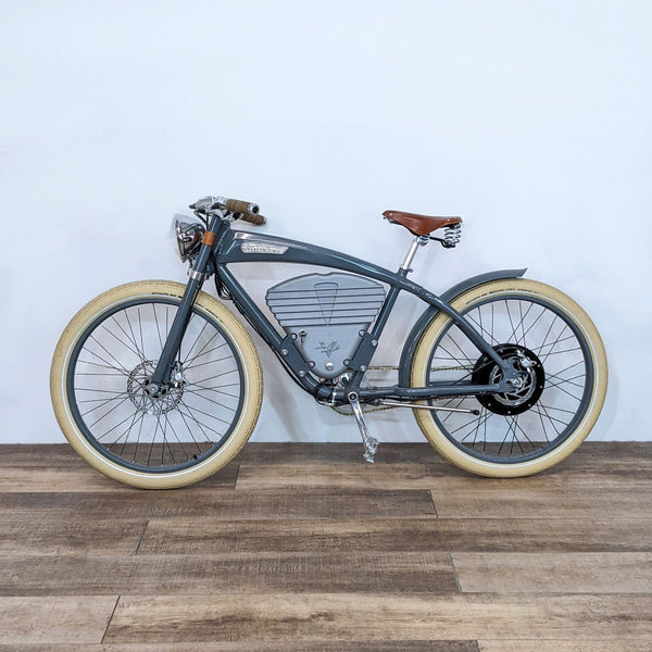 1. A side view of a Vintage Electric brand bicycle with a retro design, showcasing its grey frame and cream-colored tires on a wooden floor.