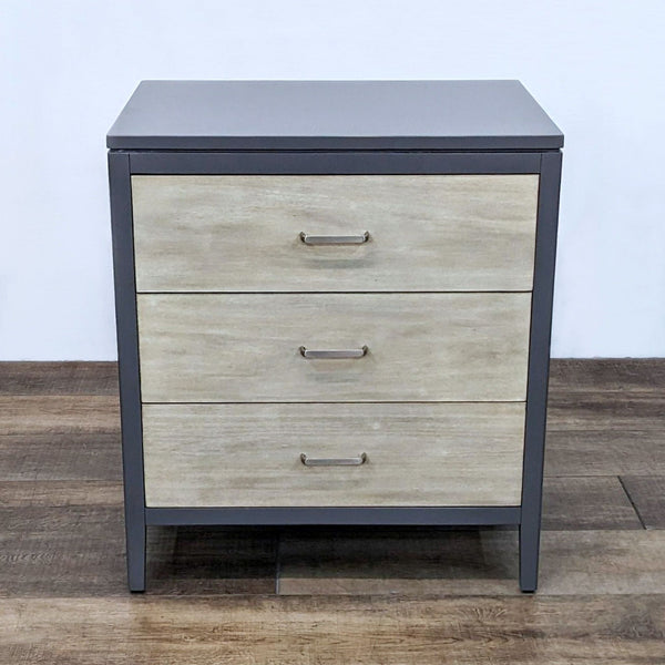Alt text 1: Ballard Designs end table, with three sandblasted wood drawer fronts and grey steel frame, closed drawers, on wooden floor.