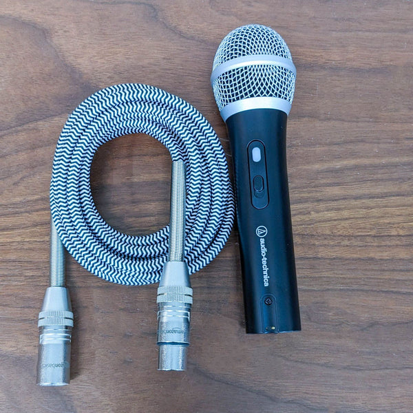 Audio-Technica microphone with dynamic transducer and cardioid pattern, USB/XLR cables on wood surface for recording/streaming.