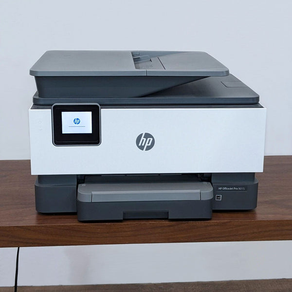 HP all-in-one printer on a desk, closed trays, compact design with HP logo on front.