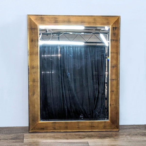 Reperch antique gold finish wood framed beveled wall mirror against a white wall, reflecting a dark curtain.