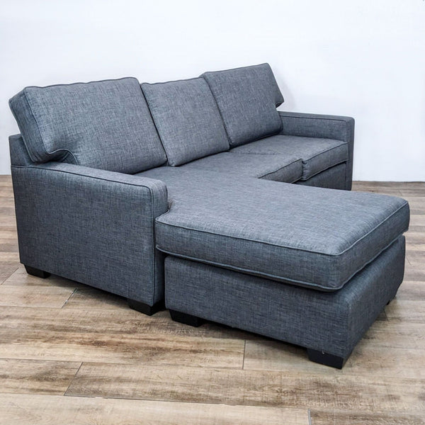 Gray Reperch sectional with reversible ottoman chaise and T back cushions on a wooden floor.