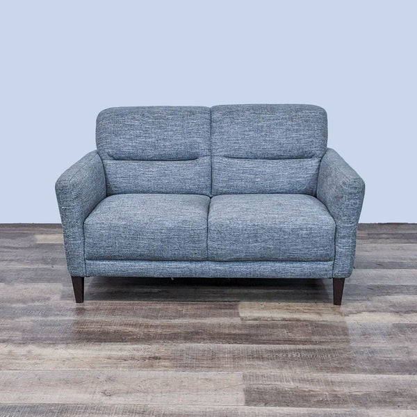 Gray Natuzzi loveseat with a tufted back, clean lines, and dark wooden feet on a wooden floor.