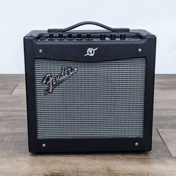 1. Front view of a portable Fender guitar amplifier on a wooden floor, showcasing its black exterior and grille with control knobs on top.