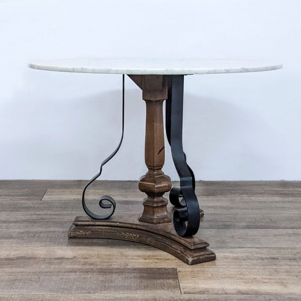 Round marble-top dining table by Reperch, with a wooden single base and metal scroll supports.