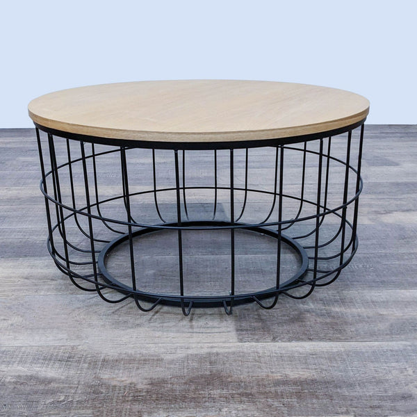Oliver Space brand coffee table with a round wood top and wireframe base, on a wooden floor.
