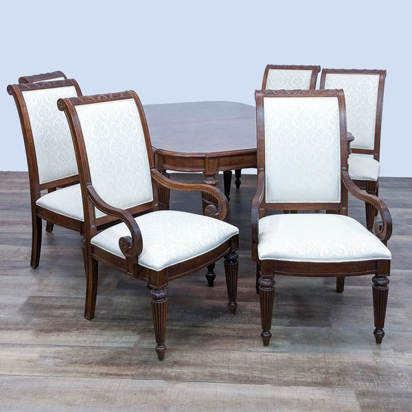 Lane extendable wooden dining table with carved legs and four upholstered chairs with patterned cushions and high backrests.