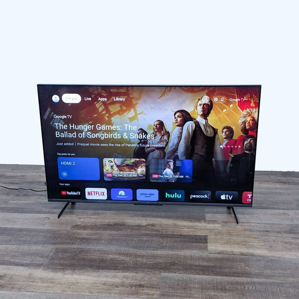 TCL Smart TV on display with vibrant Google TV interface, showing streaming apps on a minimalist stand.