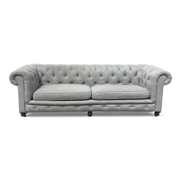 Alt text 1: Grey Chesterfield sofa with tufted upholstery, two cushions, round arms, and wooden feet from Restoration Hardware.