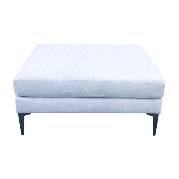 1. "Modern West Elm grey square ottoman with cast metal legs on a white background."