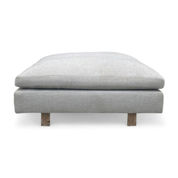 Alt text 1: Large square ottoman from West Elm with a platinum twill fabric cushion and wooden legs, suitable for use as a coffee table or bench seating.
