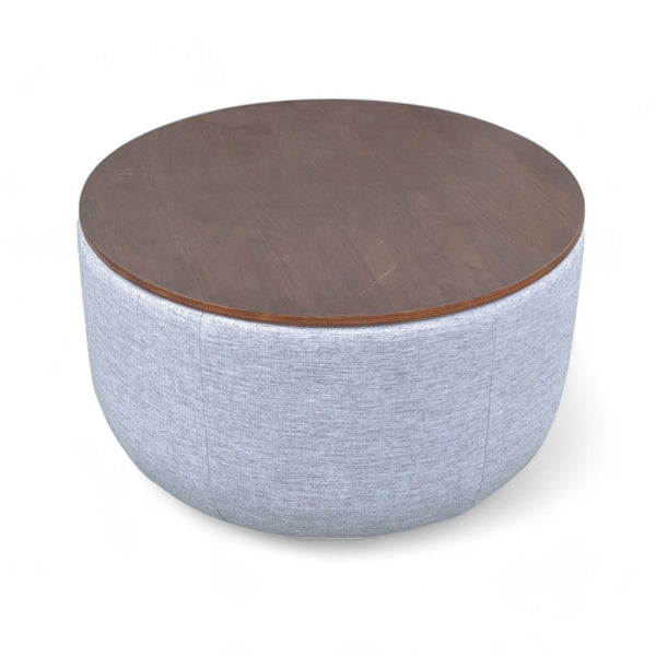 1. A round West Elm coffee table featuring an upholstered light gray base with a removable engineered wood top.