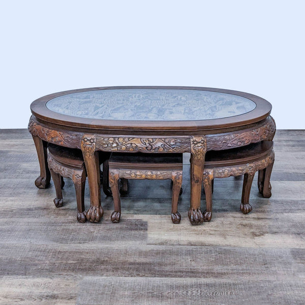 Oval-shaped solid wood Asian coffee/tea table with glass top and carved figures by Reperch, with six matching stools.