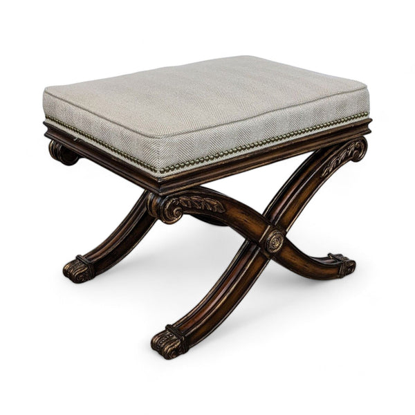 Ethan Allen neutral fabric padded ottoman with ornate wood crisscross legs and nailhead detail.