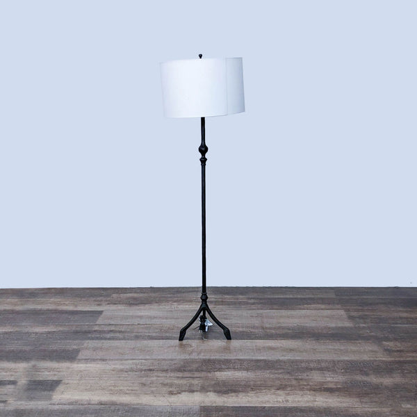 Pottery Barn floor lamp with white shade and black stand on a wooden floor against a grey background.