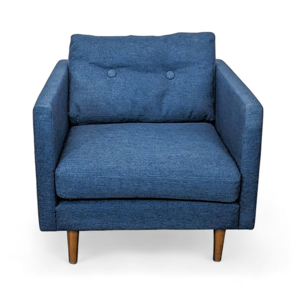 1. "Denim blue Article armchair with deep cushioning and two button tufts on backrest, featuring wooden legs, isolated on white background."