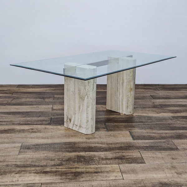 Reperch brand modern dining table with a tempered glass top and double pedestal travertine base on a wooden floor.