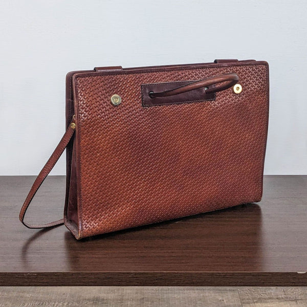 Bosca leather purse standing on a wooden surface, textured brown with top handle and side strap visible.