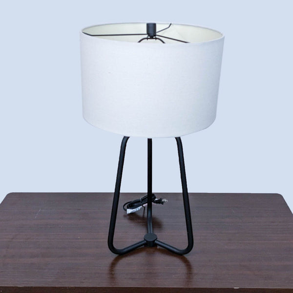 Reperch brand modern table lamp with white shade and black tripod base on a wood table.