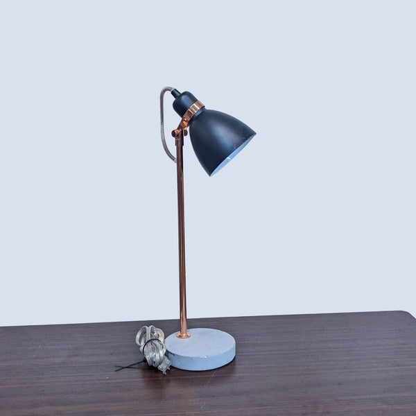 Reperch brand desk lamp with a black shade, copper stand, and concrete base on a wooden table against a white background.