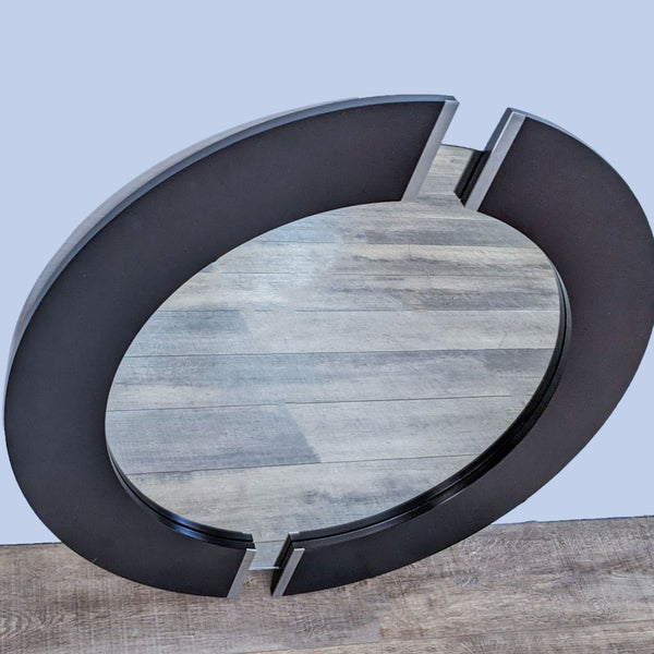Reperch round wall mirror with dark frame and silver metal accents on a wood floor.