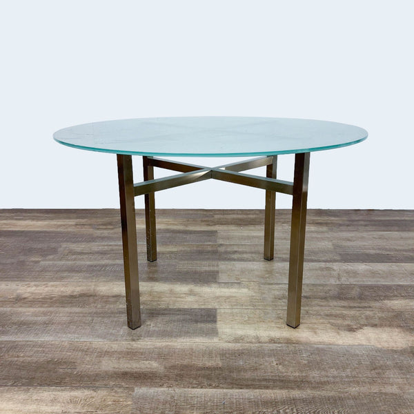 Round Benson dining table with gold metal cross brace base and frosted glass top by Room & Board.