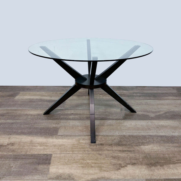 Reperch brand contemporary round dining table with dark angular wooden legs and a clear glass top, shown from an angle.