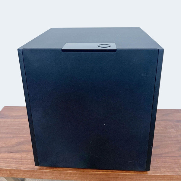 Front view of a black Triad audio subwoofer on a wooden table.