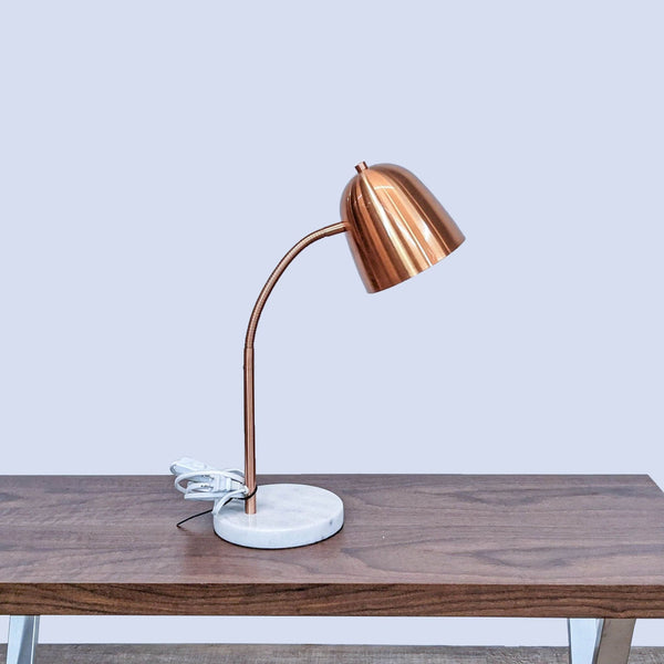 Reperch brand desk lamp with copper shade and marble base on a wooden table, turned off.