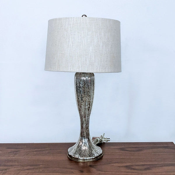 Alt text 1: A Reperch brand table lamp with a silver textured base and an off-white cylindrical shade on a wooden surface against a white wall.