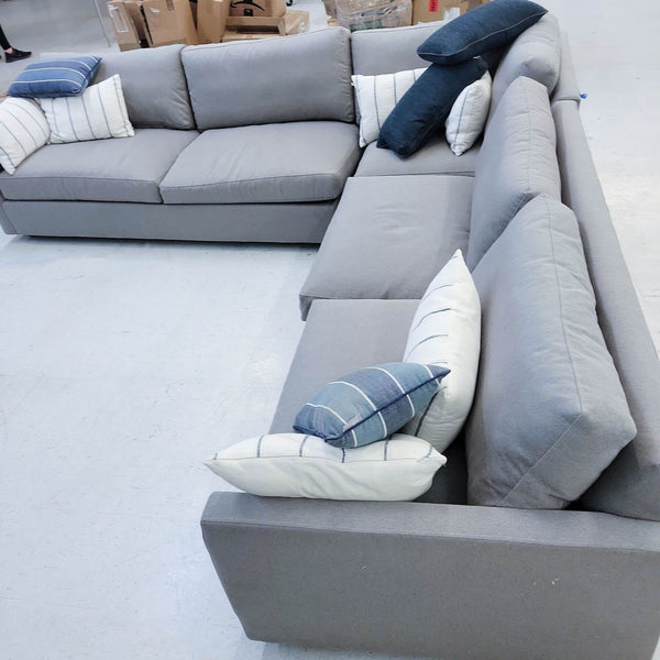 1. Room & Board brand sectional sofa in a warehouse setting, featuring gray upholstery and assorted pillows.