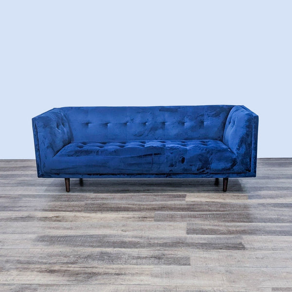 Alt text 1: Wayfair's 3-seat tufted blue velvet sofa with dark finish legs, in a modern glam style, positioned on a wooden floor.