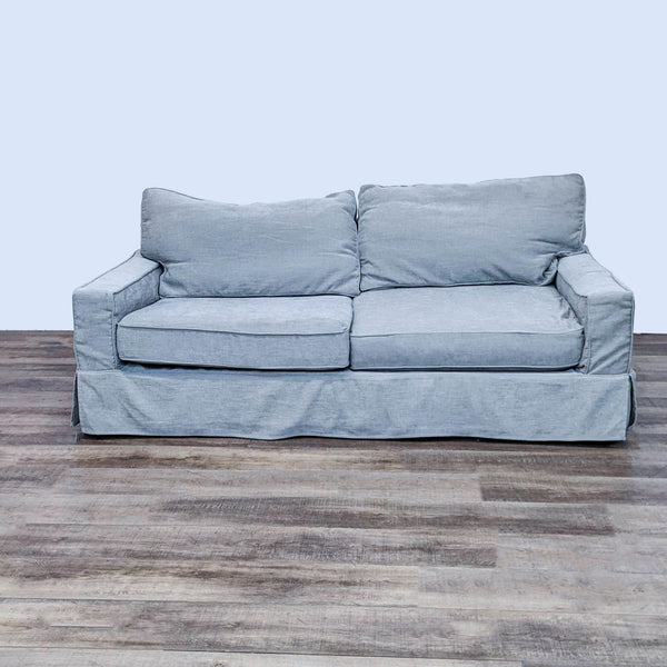 Front view of a gray fabric slipcover loveseat with track arms and T-back cushion by Pottery Barn on a wooden floor.