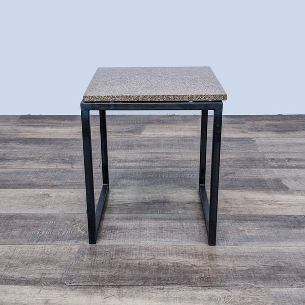 Room & Board side table with metal base and speckled top, shown in front view on a wooden floor.