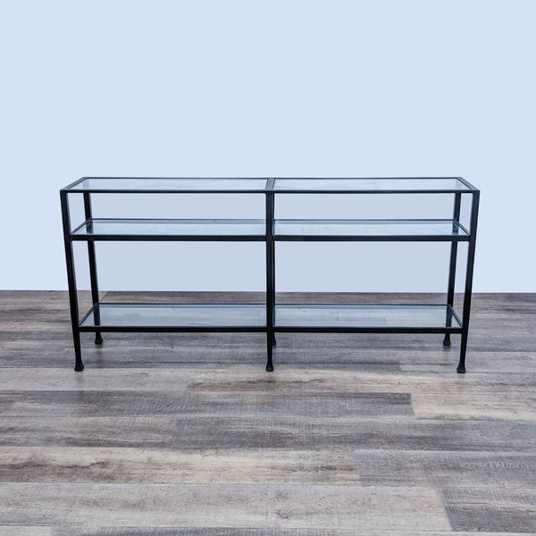 Blackened bronze wrought iron console table with tempered glass shelves by Pottery Barn, against a gray wall.
