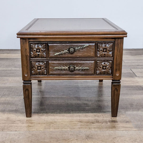 Reperch wooden end table with intricate carvings and metal handles, two drawers closed, on a hardwood floor.