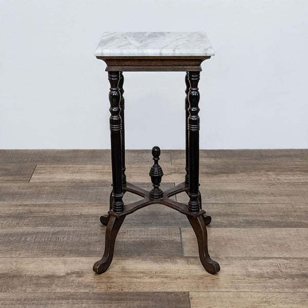 Reperch marble-topped side table with intricately turned wooden legs on a wood floor.