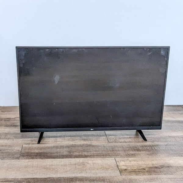 Front view of an LG Television set on a wooden floor with a blank screen.