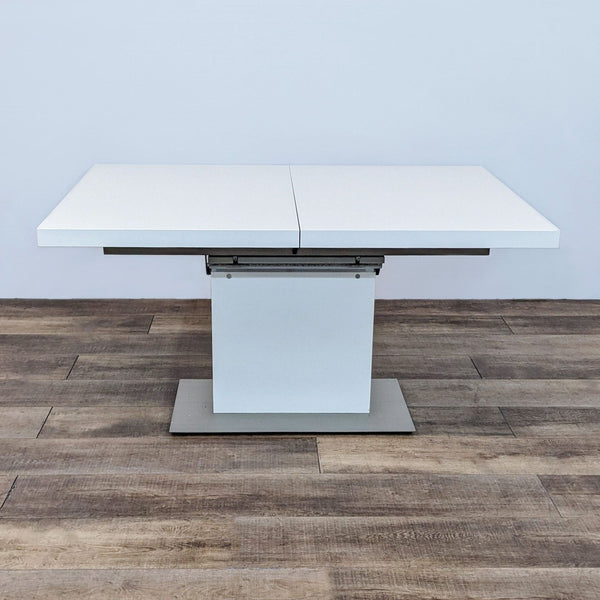 BoConcept Milano modern dining table closed, with white curved rectangular top and central stand on a wooden floor.
