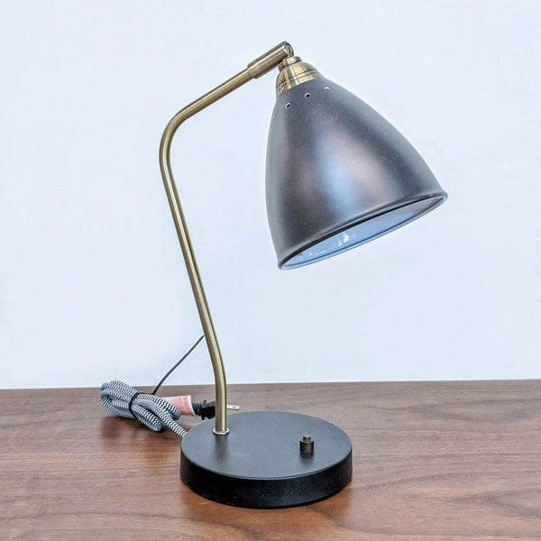Arcadia Collection desk lamp with adjustable gold neck and black shade on wood surface.