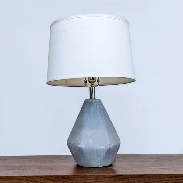 Alt text 1: Surya brand geometric table lamp with a white shade and grey faceted base on a wooden surface.