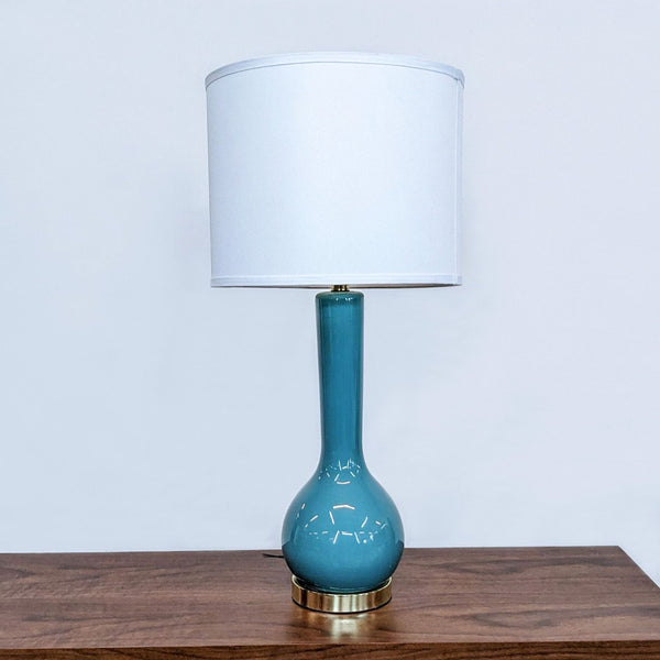 Safavieh blue ceramic table lamp with white drum shade on wooden surface against a white backdrop.
