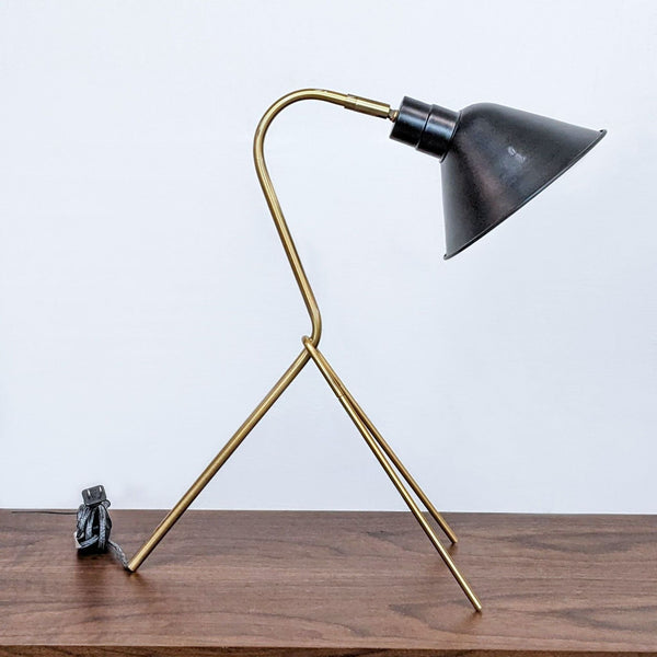 Reperch brand tripod-style desk lamp with brass legs and a black shade, placed on a wooden surface.