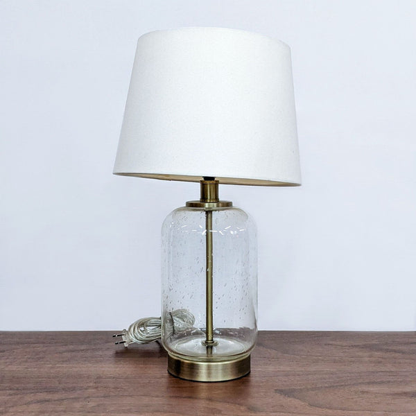 Reperch branded table lamp with a white shade and a clear, textured glass base on a wooden table.