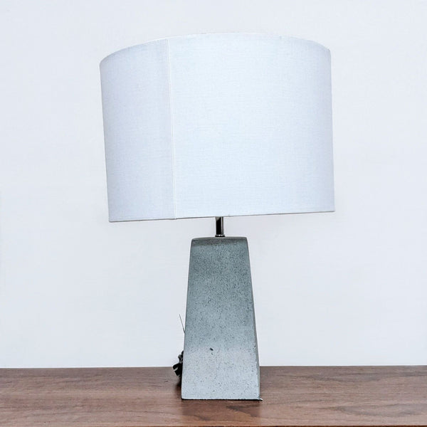 Alt text 1: A Reperch table lamp with a white fabric shade and a textured gray base on a wooden surface.