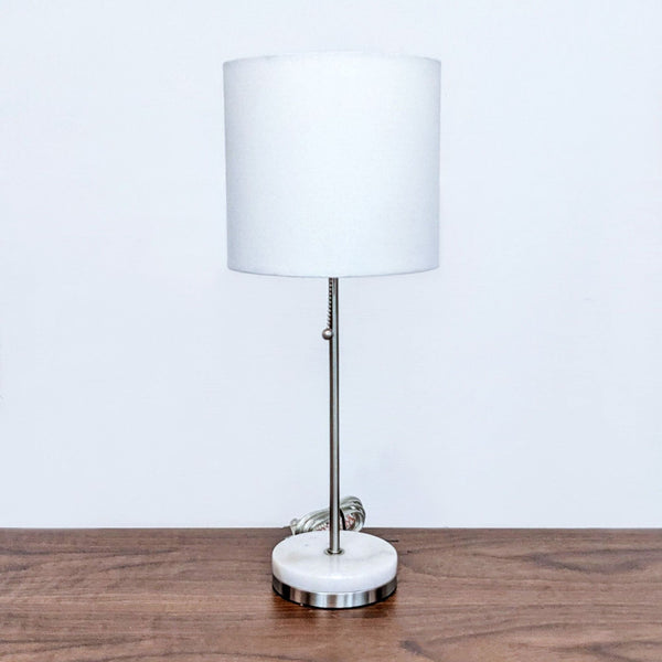 Alt text 1: Modern Reperch table lamp with cylindrical white shade and silver base on wooden surface against white wall. Max length 100.