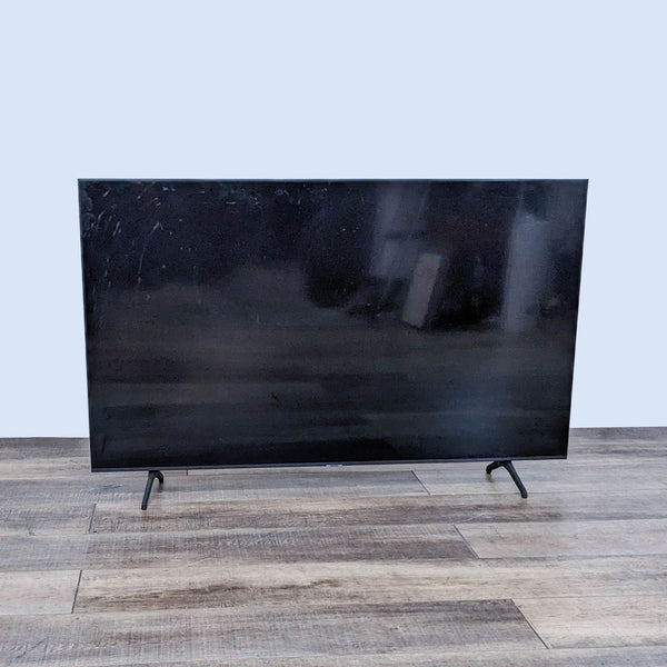 Samsung modern flat-screen TV with ultra-slim design and sturdy stand, turned off, on a wooden floor.