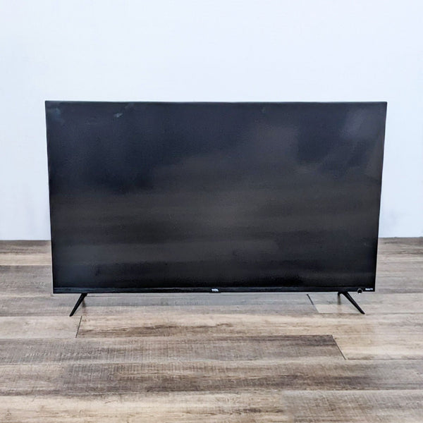 1. Sleek TCL 55S525 4K UHD TV with stand, displaying a blank screen, placed on a wooden floor against a white wall.