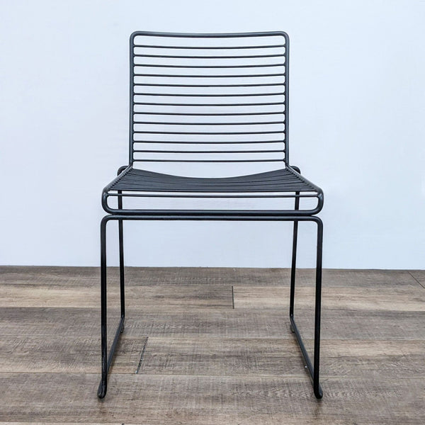 Front view of a black Hee dining chair by Hay, showcasing horizontal steel lines and powder-coated finish, on a wooden floor.